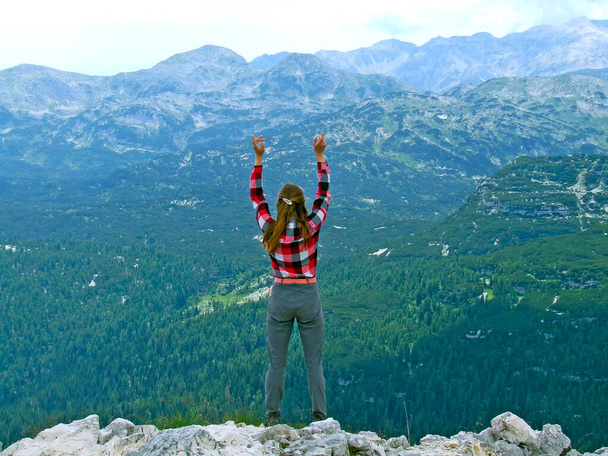 Junge Frau, die am Rand der Klippe steht und mit erhobenen Händen in den Himmel blickt. Junge Touristen freuen sich, den Gipfel des Berges zu bezwingen. Bergtourismus. Mädchen, die sich in Bergen ausruhen. Aktive Lebensweise - Foto, Bild