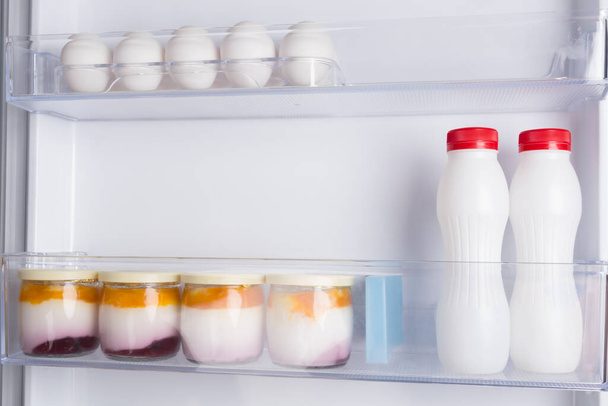 in the door of an open white refrigerator, on the shelf are yoghurts and eggs - Valokuva, kuva