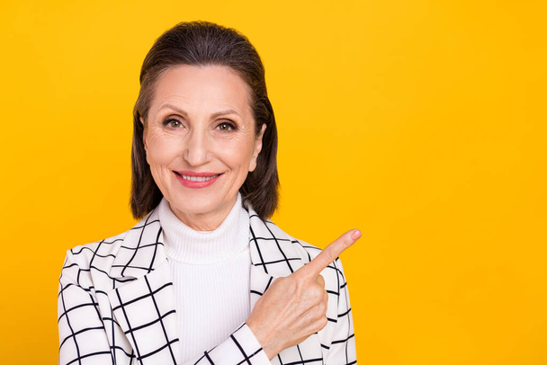 Photo of pretty cheerful aged lady indicate finger empty space promo isolated on yellow color background - Foto, imagen