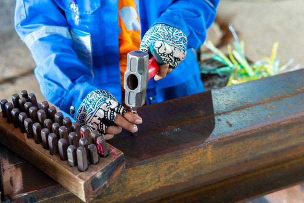Werknemer gebruiken een hamer om tekens en nummer te stempelen met stalen handstempels op stalen structuurbalk voor identificatie werkstuk. - Foto, afbeelding