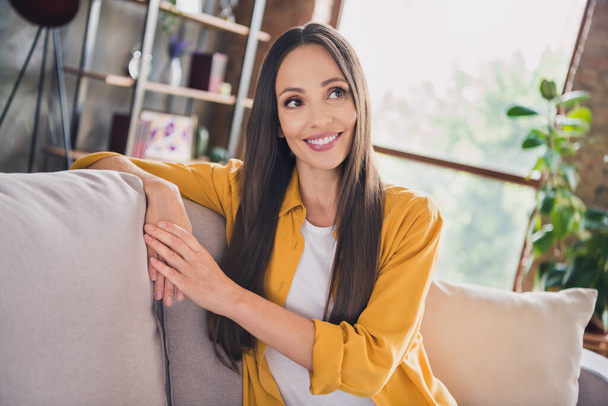 Photo of charming dreamy mature woman wear yellow shirt smiling sitting comfortable couch indoors house home room - Фото, зображення