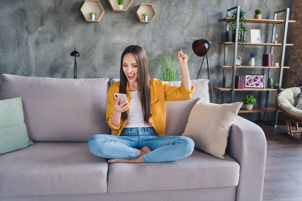 Photo of pretty lucky young lady dressed yellow shirt writing modern gadget rising fist smiling indoors room home house - Fotó, kép