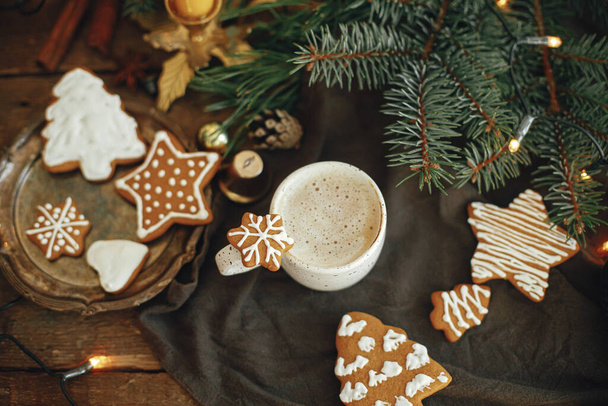 Biscotti di pan di zenzero di Natale e caffè in elegante tazza bianca, rami di abete su tovagliolo e tavolo rustico. Biscotto di pan di zenzero di fiocco di neve di Natale su caffè. Moody immagine atmosferica. Orario invernale - Foto, immagini