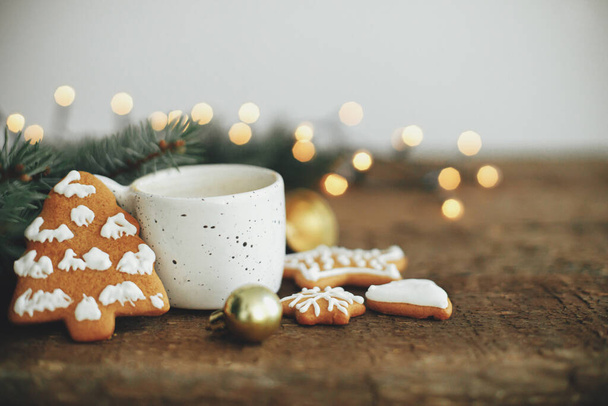 Christmas gingerbread cookies, coffee cup, fir branches on background of warm lights bokeh on rustic wooden table.  Atmospheric winter image. Seasons greeting, space for text. Merry Christmas - Foto, Bild