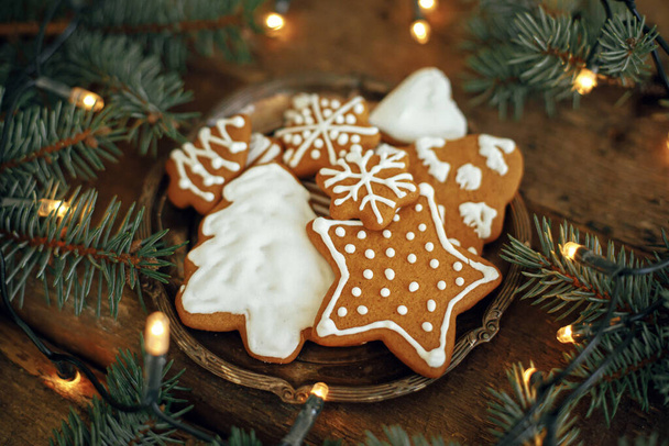 Karácsonyi mézeskalács sütik tányéron, fenyő ágak és meleg fények rusztikus fa asztalon. Légköri téli kép. Az évszakok köszöntenek. Finom házi süti. Kellemes ünnepeket! - Fotó, kép
