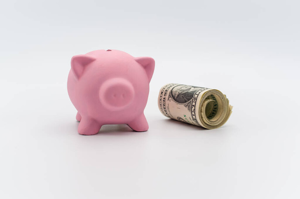 a cute pink piggy bank with a banknotes wad on a white tabletop with copy space - Foto, imagen