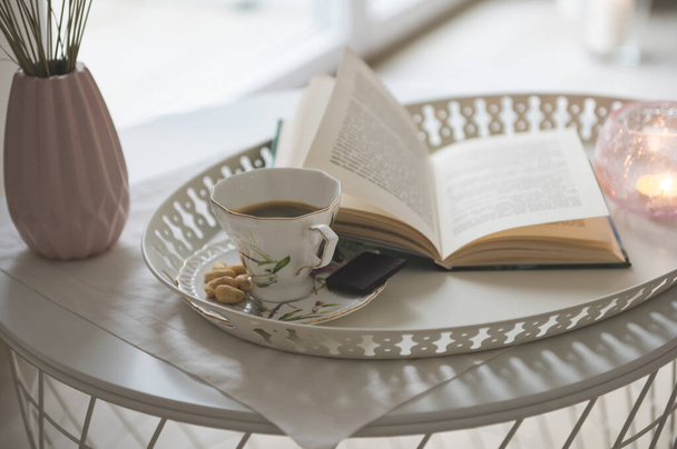 Photo of stylish white tray with black koffee and dark chocoltte and a book. Cozy chair on background - Foto, imagen