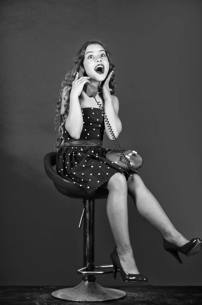 retro girl speak on phone. pretty kid talking on vintage telephone. pinup girl happy conversation. surprised kid sit on chair dial phone. communication concept. retro style. shopping online - Fotoğraf, Görsel