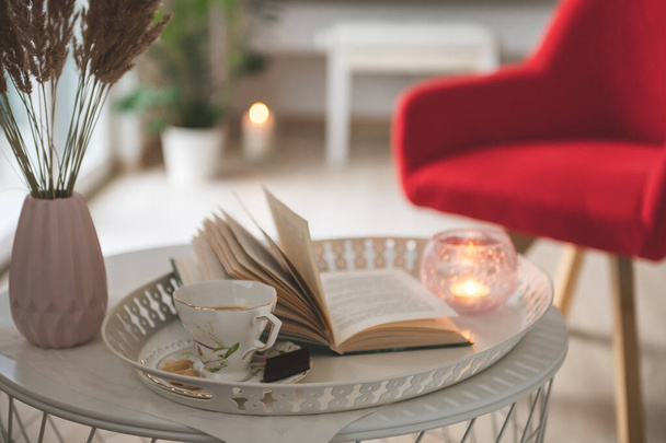 Photo of stylish white tray with black koffee and dark chocoltte and a book. Cozy chair on background - Zdjęcie, obraz