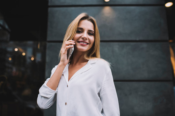 Content young lady with dyed long hair wearing elegant blouse looking at camera and standing outdoors while listening to colleague phoning - Φωτογραφία, εικόνα