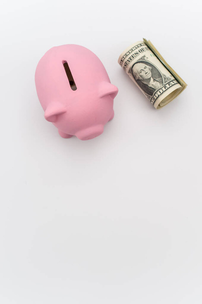 a cute pink piggy bank with a banknotes wad on a white tabletop with copy space - Φωτογραφία, εικόνα