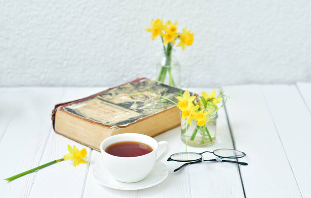 Відкрита стара книга, "Кубок чаю і жовті даффіли на легкому дерев'яному фоні". Весняна затишна ранкова .Copy простір. Вибіркове зосередження - Фото, зображення
