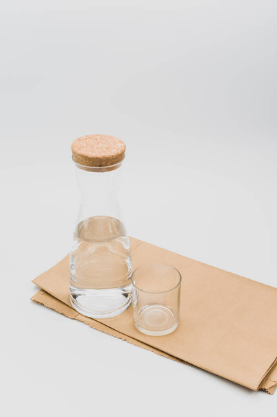 γυάλινη φιάλη γεμάτη με καθαρό νερό σε λευκό φόντο και χαρτί τροφίμων με χώρο κειμένου - Φωτογραφία, εικόνα