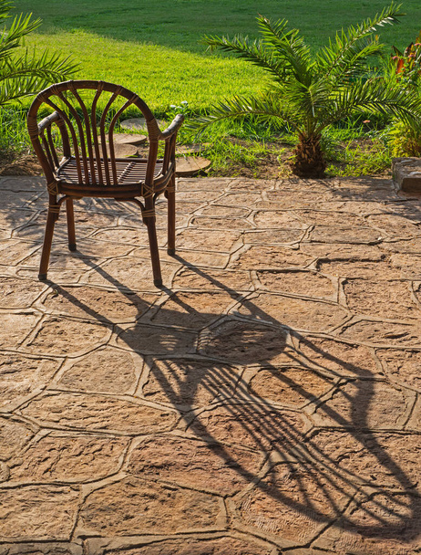 Abstraktní zátiší dřevěné židle v venkovní zahradě s dlouhým stínem vrhaným přes kamennou dlažbu terasu terasa - Fotografie, Obrázek