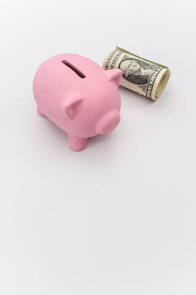 a cute pink piggy bank with a banknotes wad on a white tabletop with copy space - Foto, immagini