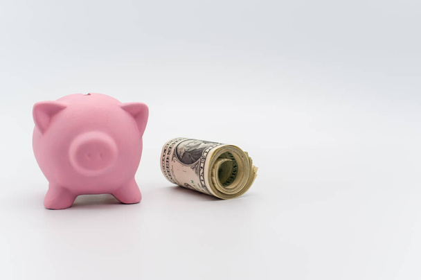 a cute pink piggy bank with a banknotes wad on a white tabletop with copy space - Photo, image