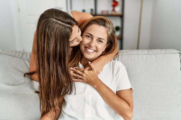 Mother and daughter kissing and hugging each other sitting on sofa at home - Fotó, kép