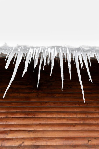 Icicles formado en el techo de la casa. Día soleado de invierno. La nieve está empezando a derretirse.. - Foto, imagen