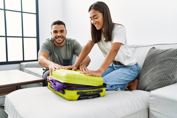 Latino hombre y mujer pareja sonriendo confiado cerca viaje maleta en casa - Foto, imagen