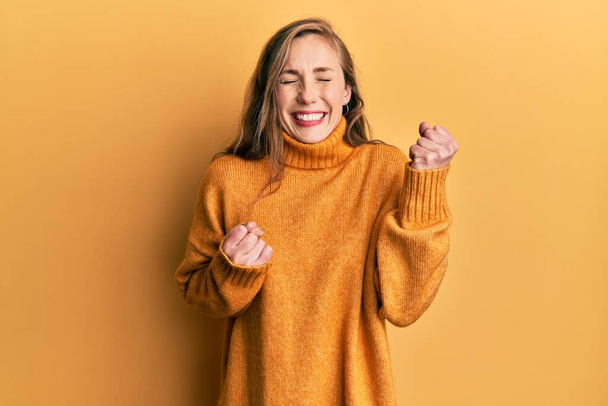 Mujer rubia joven vistiendo ropa casual celebrando sorprendida y sorprendida por el éxito con los brazos levantados y los ojos cerrados  - Foto, imagen