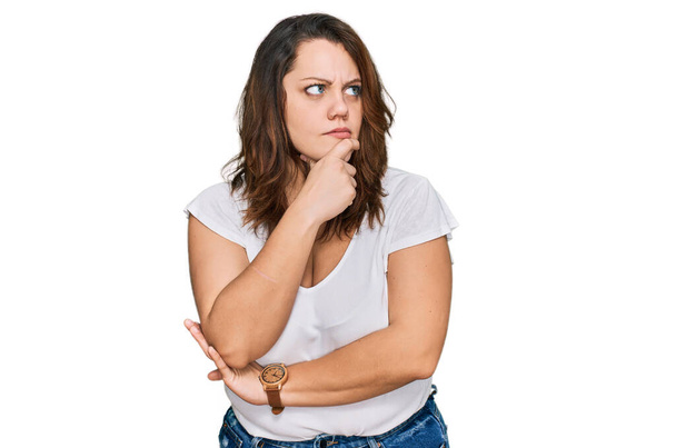 Молодая женщина плюс размер носить случайные белые футболки думая о вопросе, обеспокоенный и нервный с рукой на подбородке  - Фото, изображение