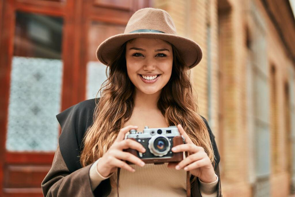Молодая испаноязычная туристка улыбается счастливой, используя винтажную камеру в городе. - Фото, изображение
