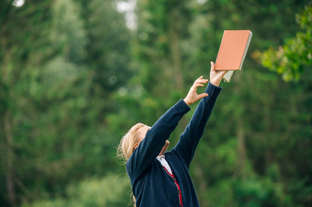 School girl holding  books up in the sky. Outdoor. Education, knowledge, back to school, first day at school concept. Young girl holding bible and lift up hand with light background,christian concept - Photo, Image
