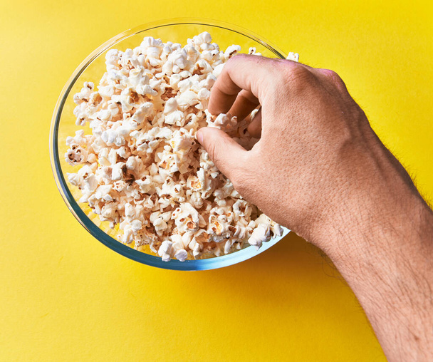  Käsi tilalla suolainen popcornia kulhoon keltaisella pohjalla - Valokuva, kuva