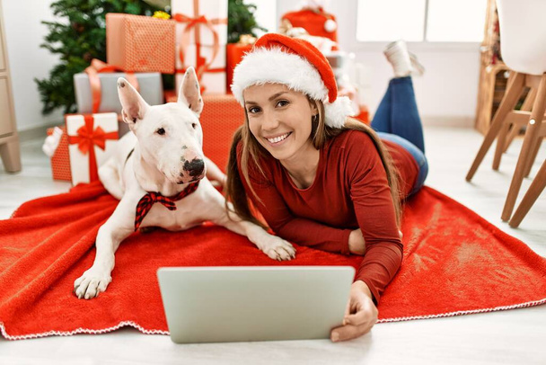 Genç beyaz kadın evde köpekle birlikte yatan bir dizüstü bilgisayar kullanıyor. - Fotoğraf, Görsel