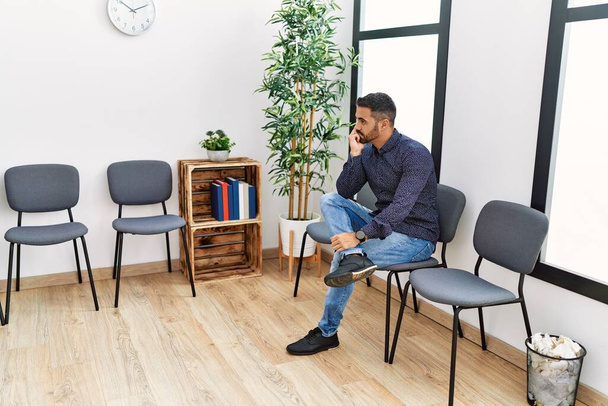 Young hispanic man desperate sitting on chair at waiting room - Foto, Imagen