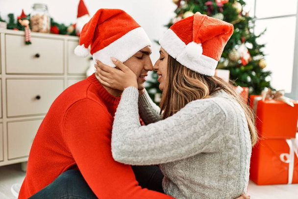 Młoda para w świątecznym kapeluszu i całowaniu. Siedząc na podłodze przytulając się w domu. - Zdjęcie, obraz