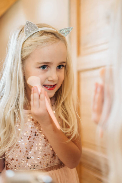 Милая маленькая девочка, играющая с косметикой, смотрящей в зеркало. Маленькая девочка держит порох макияж кисти - Фото, изображение
