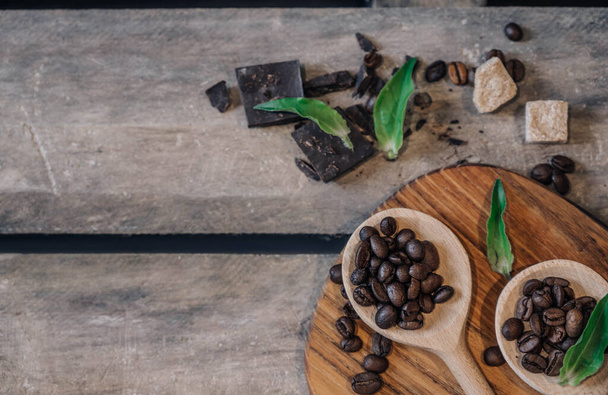 Houten lepels met verschillende soorten koffiebonen, pure chocolade en bruine suiker op donkere vintage rustieke houten ondergrond. Zijaanzicht. - Foto, afbeelding