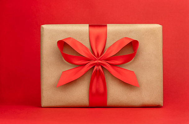 Wrapped present box with red ribbon to a celebration on a red backgroun - Фото, зображення