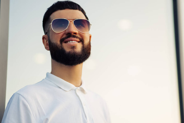 Portrait of a fashionable young man in the city, a man in a white T-shirt posing in the street in sunglasses, the concept of style, vogue, fashion - Фото, зображення