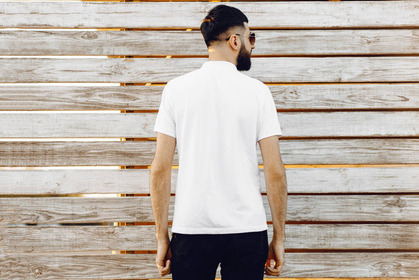Shirt design and people concept. Stylish man in blank white t-shirt from behind, man in white t-shirt on wooden wall background. White t-shirt template. Back view. Mock up template for print design - Foto, Imagen