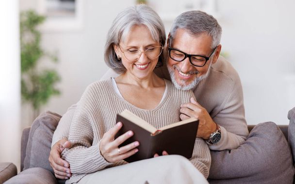 gelukkig glimlachen senior familie paar in liefde lezen boek samen thuis - Foto, afbeelding
