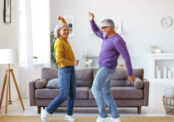Energetische senior familie paar dansen samen in de woonkamer thuis, verhuizen naar muziek - Foto, afbeelding