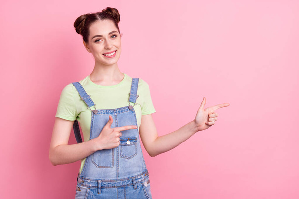 Photo portrait girl in overall pointing empty space smiling recommending isolated pastel pink color background - Foto, afbeelding