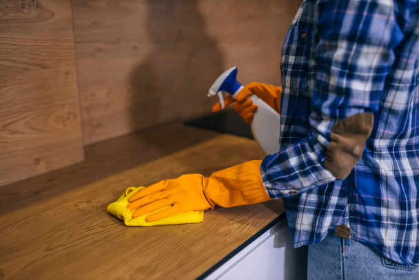 Концепция чистоты. Женская рука в оранжевой перчатке держит мягкую тряпку, вытирает деревянный стол из пыли и грязи. Очистка дома, мытье ламината. - Фото, изображение