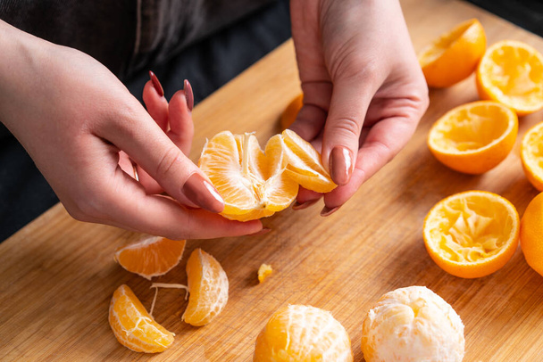 Женские руки чистят и ломают спелый мандарин, готовят домашний сок. - Фото, изображение