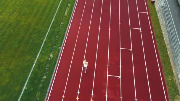 Воздушный беспилотный снимок спортсмена, бегущего на короткое расстояние на стадионе. Спортсменка бегает на красных беговых дорожках - Кадры, видео