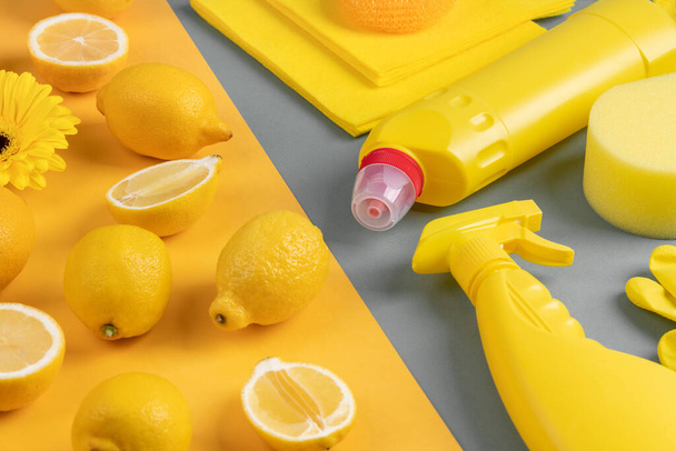 Fresh yellow lemons, lemon halves, gerbera flower, household chemicals and cleaning tools, spring cleaning concept. - Photo, Image
