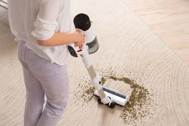 Young woman uses cordless vacuum cleaner to clean home carpet. Close-up of mung bean brush from carpet. - Photo, image