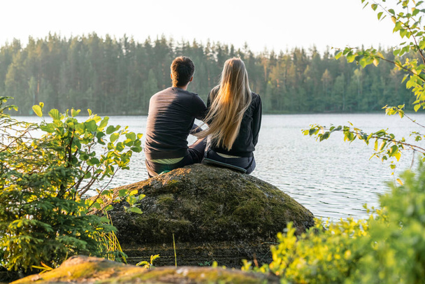 Loving young couple man and woman sit on stone near evening lake. Psychology of relationships. Gender psychology. Blured foreground. - 写真・画像