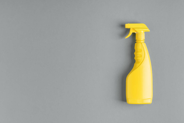 Yellow plastic bottle of spray with household chemicals in liquid form for cleaning and cleaning premises on a gray background. The concept of minimalism and popular colors. - Foto, imagen