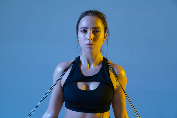 Serious athletic young woman looking camera and holding rope on her shoulders. - Фото, зображення