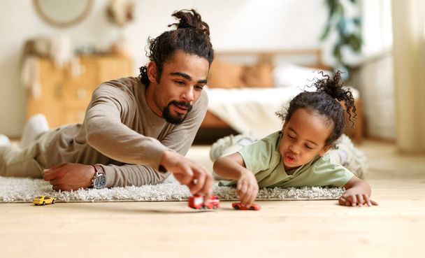 幸せなアフリカ系アメリカ人の家族の父と子供の息子は家で一緒におもちゃをプレイしながら笑う - 写真・画像