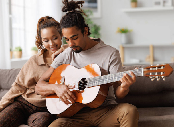 Młody uśmiechnięty Afrykanin amerykański mężczyzna muzyk gra instrumentalną muzykę na gitarze dla szczęśliwej dziewczyny - Zdjęcie, obraz