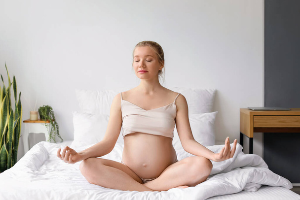 Young pregnant woman meditating on bed at home - Foto, Imagen